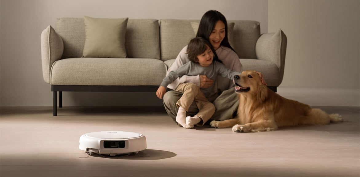 Robot sprzątający DJI ROMO S odkurza a obok na podłodze siedzi kobieta z dzieckiem i psem